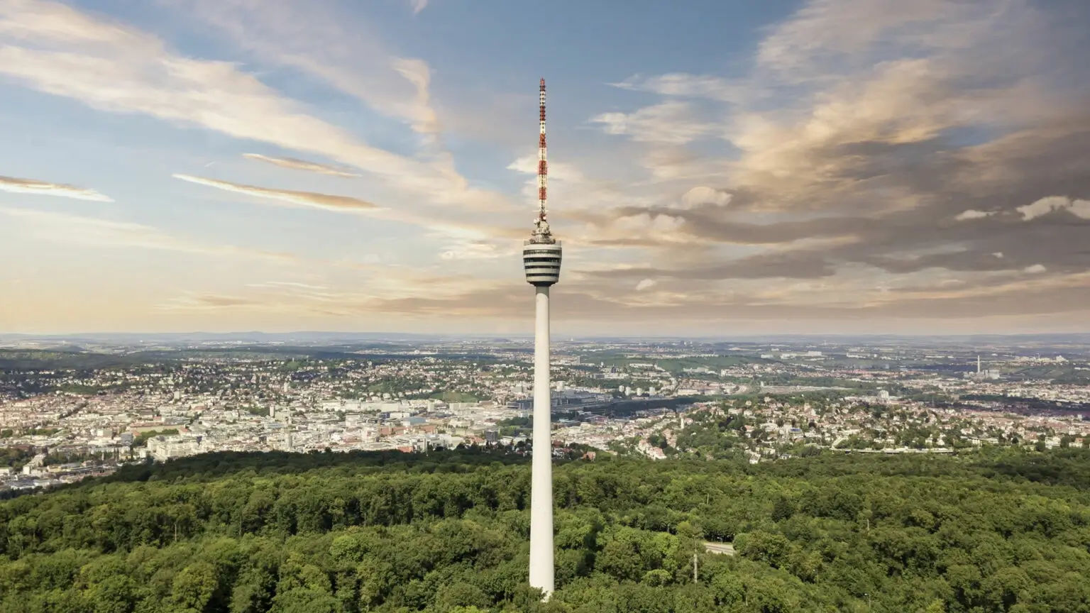 Der Stuttgarter Fernsehturm ragt aus grunem Wald vor der Stadtkulisse empor